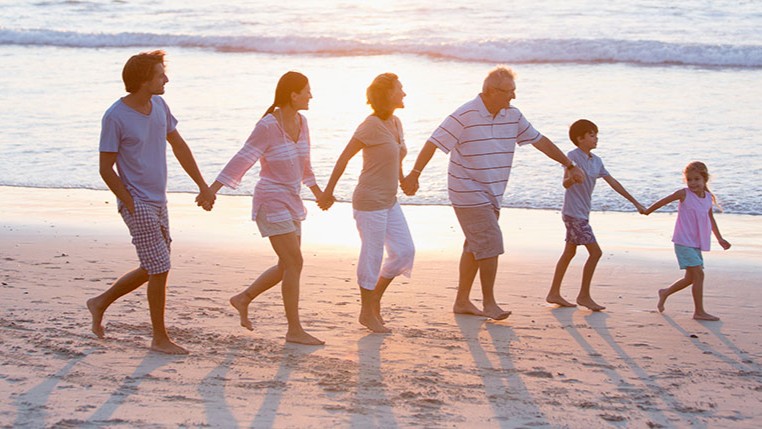 Famille de trois générations main dans la main sur la plage, transmission de patrimoine et assurance-vie